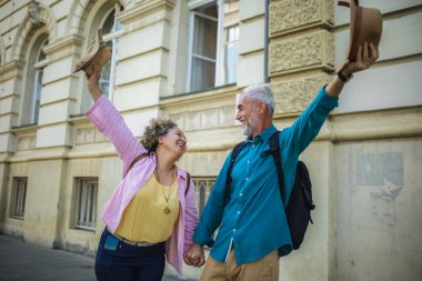 Şehir merkezinde mutlu mesut ayakta duran yaşlı evli bir çift. Havaya şapka atmak..