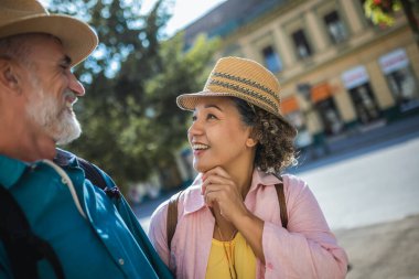 Yaşlı evli çift el ele tutuşup yeni şehirde yürüyor. Sırt çantaları ve şapkaları var. Keşif ve seyahat konsepti.