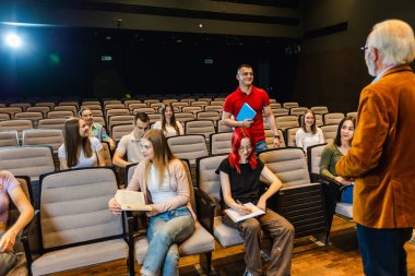 Erkek öğrenci ayakta ve yaşlı profesörünün sorularını cevaplıyor..
