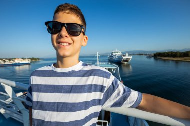 Güneş gözlüklü, martılarla çevrili bir çocuk güzel manzaralı bir feribotta dinleniyor..