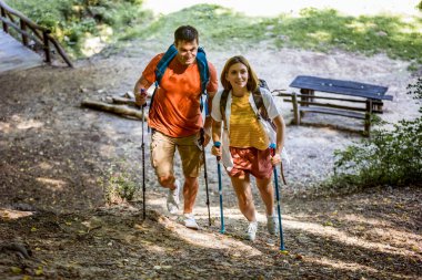 Evli çift ormanda yürüyüş direkleri ve diğer yürüyüş ekipmanlarıyla yürüyüş yapıyor..