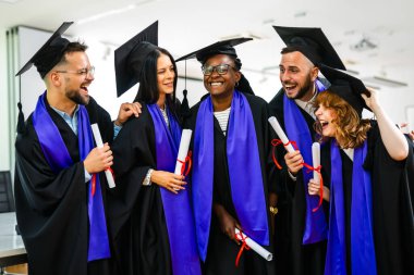 Toga giymiş ve diplomalarını elinde tutan mutlu çok ırklı öğrenci grubu..