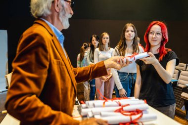 Yaşlı erkek öğretmen, amfitiyatroda kızıl saçlı kız öğrenciye diploma veriyor..