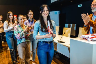 Amfitiyatroda kadın öğrenciye diploma veren yaşlı bir erkek öğretmen..