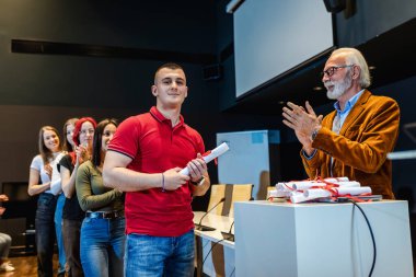 Yaşlı erkek profesör, bir yılın sonunda sıkı çalışan öğrenciye diploma verdi..