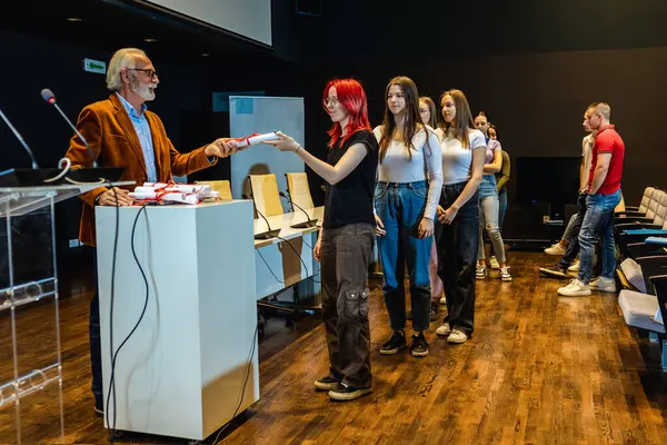 Yaşlı erkek öğretmen, amfitiyatroda kızıl saçlı kız öğrenciye diploma veriyor..