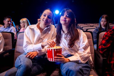 Two best friends are watching a movie in cinema and they are eating popcorn. clipart