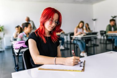 Çalışması için kitaplardan notlar alan odaklanmış genç bir öğrenci. Üniversite öğrencisi masada oturuyor ve çalışıyor..