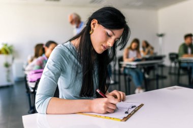 Çalışması için kitaplardan notlar alan odaklanmış genç bir öğrenci. Üniversite öğrencisi masada oturuyor ve çalışıyor..
