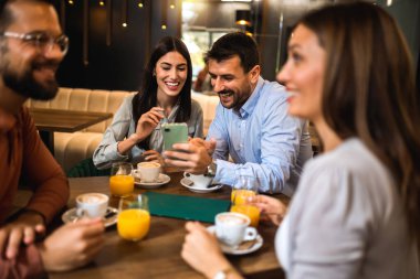 Arkadaşlarla kafede buluştuk. Kahve ve portakal suyu içiyorum. Adam telefonunda sevgilisine bir şey gösteriyor.