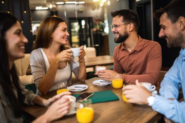 Bir grup arkadaş kafede buluştu. Kahve ve portakal suyu içiyorum. Kız ve erkek konuşurken diğer arkadaşlar onları dinliyor..