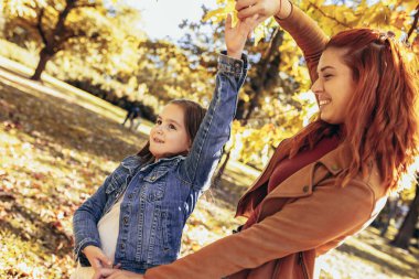 Kızıl anne, kızıyla renkli parkta eğleniyor. Sonbahar günü.