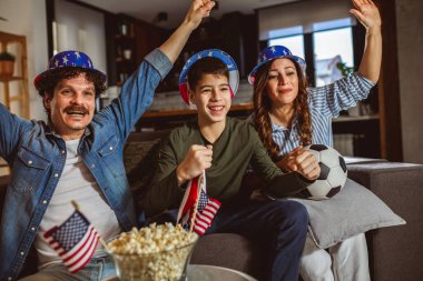 Latin ailesi Amerikan bayraklarıyla futbol maçı izliyor.