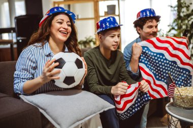 Latin ailesi Amerikan bayraklarıyla futbol maçı izliyor.