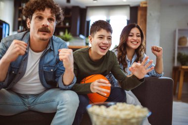 Latin ailesi basketbol maçı izliyor ve patlamış mısır yiyor. Takımları için tezahürat yapıyorlar..