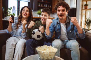 Latin ailesi futbol maçı izliyor ve patlamış mısır yiyor. Takımları için tezahürat yapıyorlar..