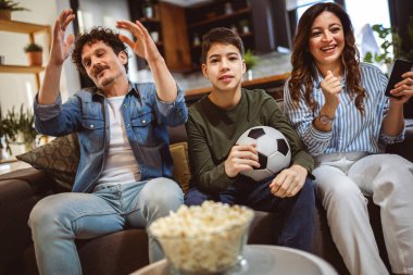 Latin ailesi futbol maçı izliyor ve patlamış mısır yiyor. Takımları kaybediyor diye üzülüyorlar..