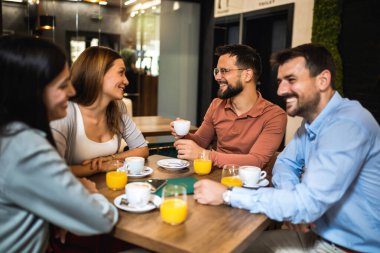 Bir grup arkadaş kafede buluştu. Kahve ve portakal suyu içiyorum. Kız ve erkek konuşurken diğer arkadaşlar onları dinliyor..
