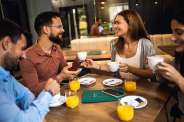 Bir grup arkadaş kafede buluştu. Kahve ve portakal suyu içiyorum. Kız ve erkek konuşurken diğer arkadaşlar onları dinliyor..