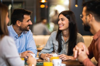 Bir grup arkadaş kafede buluştu. Kahve ve portakal suyu içiyorum. Kız ve erkek konuşurken diğer arkadaşlar onları dinliyor..