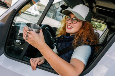 Genç kızıl kadın enerji toplayabilmek için uzun bir araç kullanıyor ve kahve içiyor..