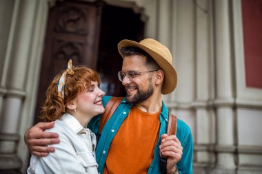 Yeni şehri keşfeden genç bir çift. Sarılmak ve ortada yürümek. Şapkalar ve sırt çantaları takıyor..