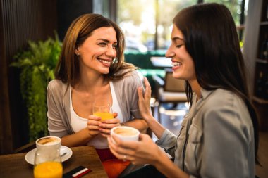 İki kız arkadaş takılmak, dedikodu yapmak ve birbirleriyle konuşmak için kahve dükkanında buluştular. Kahve ve portakal suyu içiyorlar..