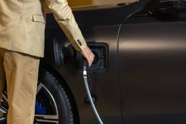 Şarj istasyonundaki genç işadamı elektrikli arabasını şarj etmek için fişi tutuyor. Eko elektrikli araba konsepti