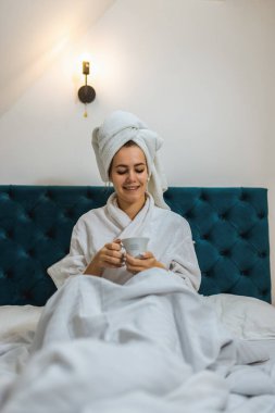 Otel odasında bir kadın. Kafasında bornoz ve havlu vardı. Banyodan sonra sıcak bir şeyler içmek..