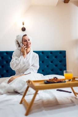 Otel odasında kafasında bornoz ve havluyla telefonda konuşan güzel bir kız..