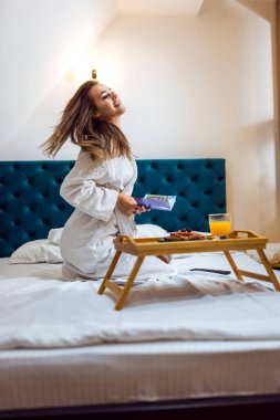 Otel odasında bornozlu, kitap okuyan güzel bir kız..