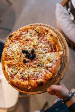 Pizza on a wooden board is served by a waiter in a restaurant. Delicious looking pizza. Food and drink concept. clipart