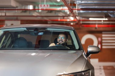 Genç işadamı yeraltı garajında park yeri arıyor. Arabasıyla geziyor..