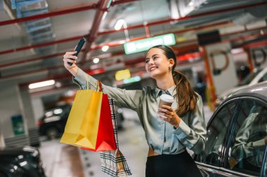 Young woman standing by her car after shopping with bags taking selfie. clipart