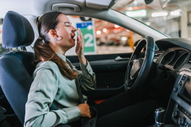 Arabasında esneyen genç bir kadın. Otoparkta dolaşmaktan yoruldum..