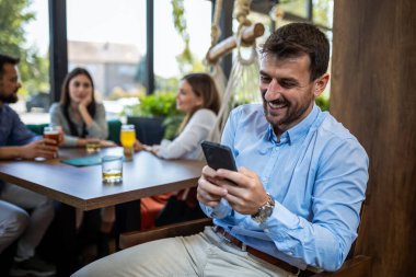 Genç işadamı restoranda arka planda arkadaşlarıyla telefonunu kullanıyor..