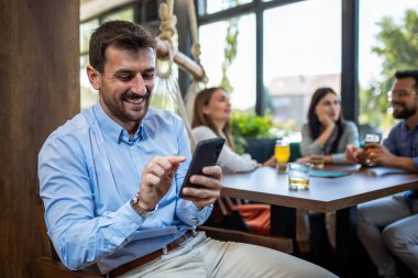 Genç işadamı restoranda arka planda arkadaşlarıyla telefonunu kullanıyor..