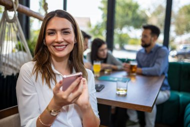 Restoranda telefonunu kullanan bir kadın. Arka planda arkadaşları var..