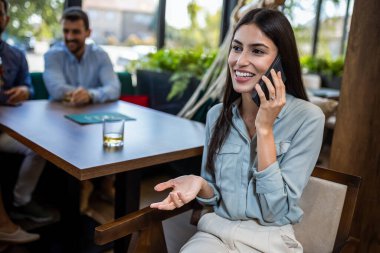 Arkadaşları arka plandayken restoranda telefonla konuşan bir kadın..