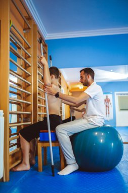 Küçük çocuğun terapi amaçlı kinezi terapisi. Çocuk yapışırken ve egzersiz topuna otururken leğen kemiğini düzeltiyorum. Bir kayropraktör ona yardım ediyor..
