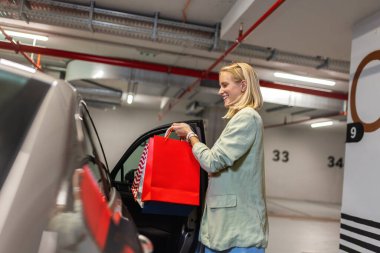 Young woman unlocking door of her car to put bags after shopping. clipart