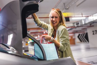 Young woman unlocking trunk of her car to put bags after shopping. clipart