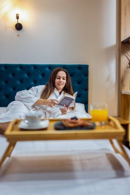 Otel odasında bornozlu, kitap okuyan güzel bir kız..