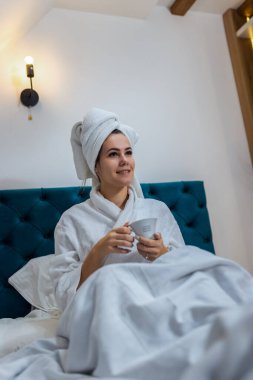 Otel odasında bir kadın. Kafasında bornoz ve havlu vardı. Banyodan sonra sıcak bir şeyler içmek..