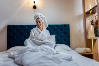 Otel odasında bir kadın. Kafasında bornoz ve havlu vardı. Banyodan sonra sıcak bir şeyler içmek..