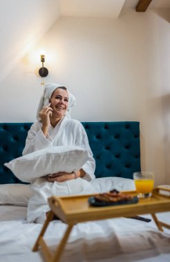 Otel odasında bornozlu, telefonda konuşan güzel bir kız..