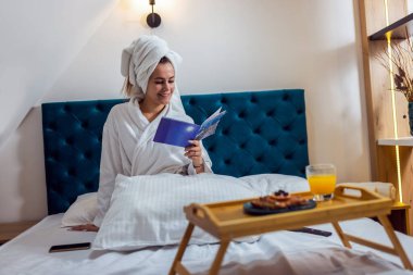 Otel odasında bornozlu, kitap okuyan güzel bir kız..