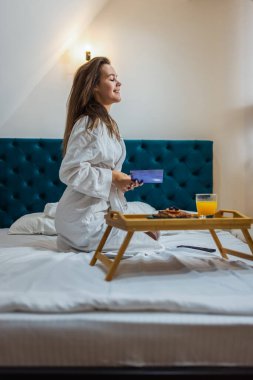 Otel odasında bornozlu, kitap okuyan güzel bir kız..