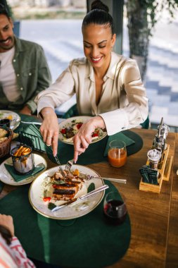 Güzel bir kadın arkadaşlarıyla bir restoranda öğle yemeği yer. Salatayla et yiyor..