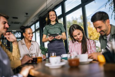 Garsondan yemek sipariş eden bir grup insan. Garson tablete emirler yazıyor. Garson onlara yardım ederken kararsız insanlar menüyü okuyor..
